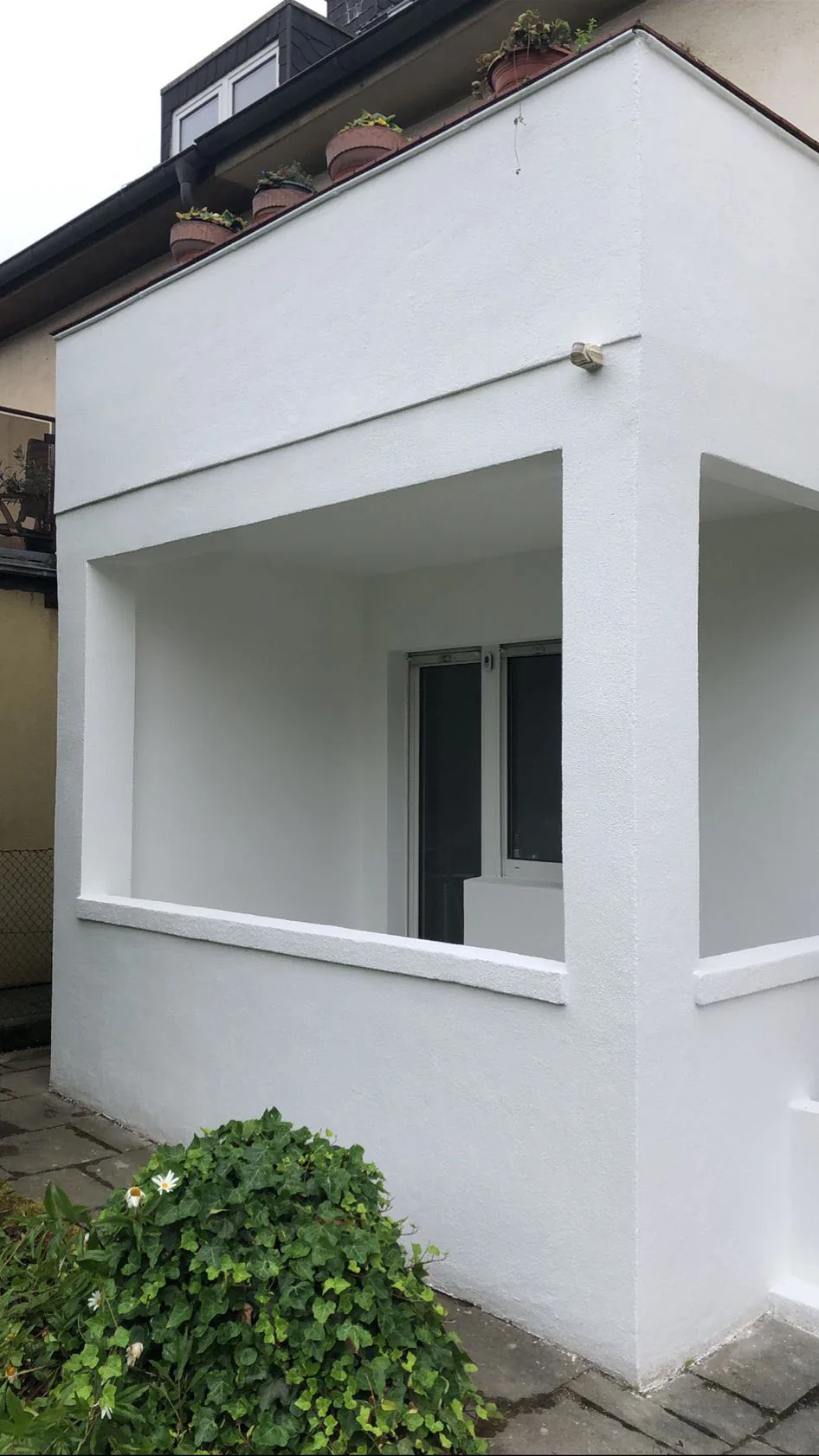 Weiß verputzter und gestrichener Anbau mit Terrasse an einem Wohnhaus.