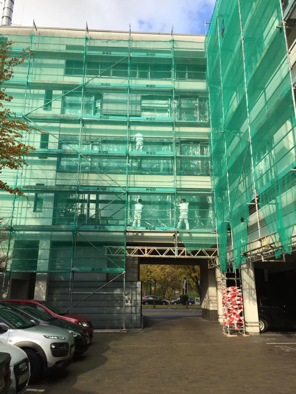 Eingerüstetes Bürogebäude mit grünem Schutznetz, Maler arbeiten auf mehreren Etagen.
