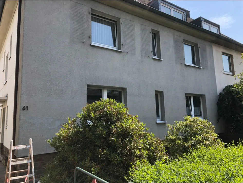 Hausfassade vor dem Anstrich: grauer, fleckiger Putz mit Hausnummer 61.