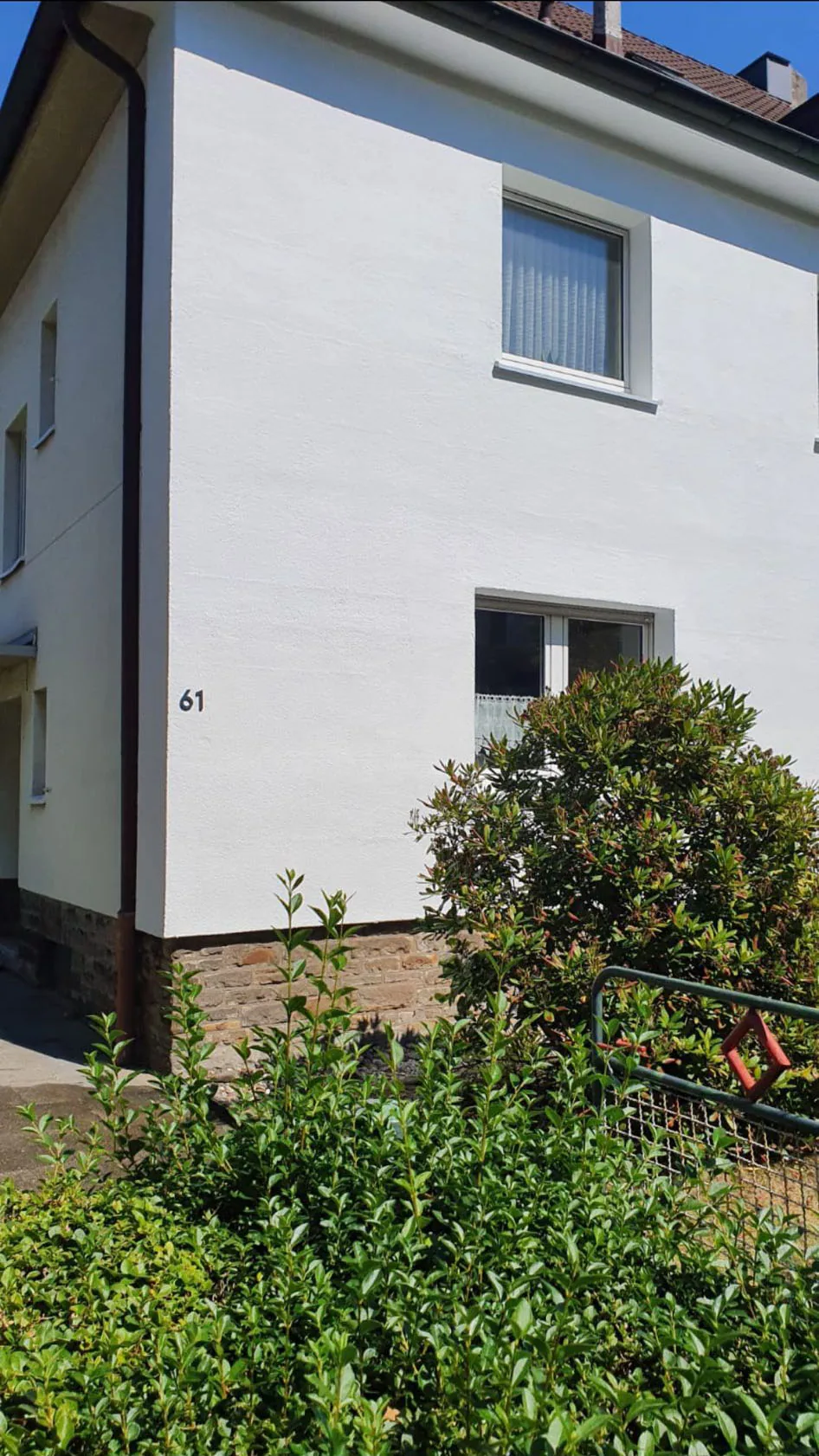 Dieselbe Hausecke nach dem Anstrich: strahlend weiße Fassade mit Hausnummer 61.