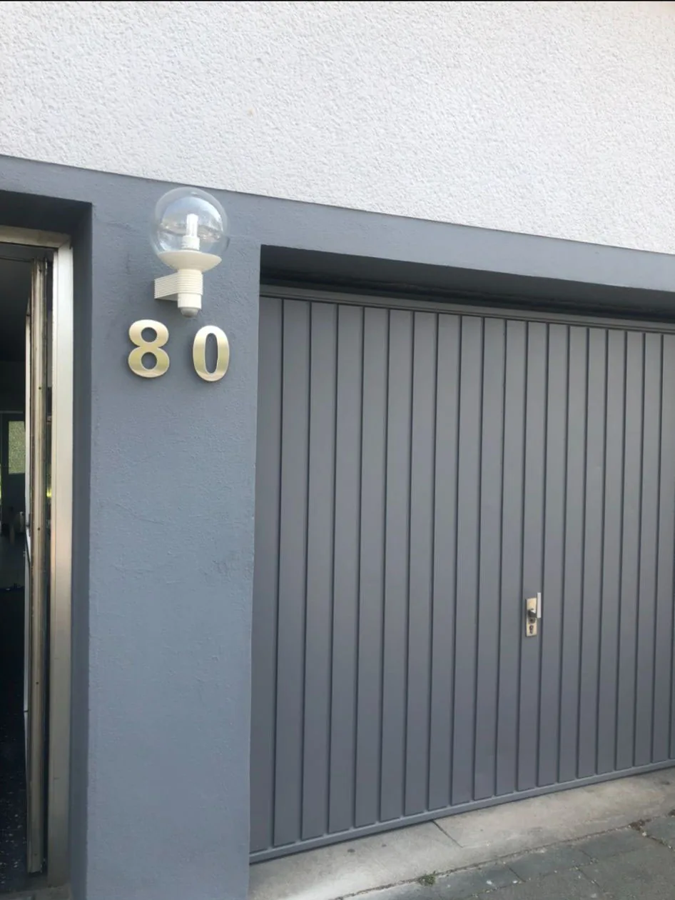 Garagentor und Torrahmen frisch in Grau lackiert, Hausnummer 80 in Edelstahl.