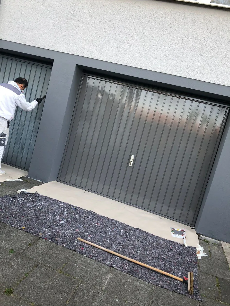 Maler lackiert ein Garagentor, Boden mit Malervlies abgedeckt.