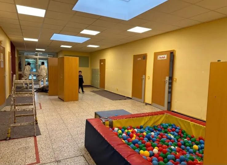 Flur einer Kindertagesstätte mit gelb gestrichenen Wänden und Bällebad, Maler im Hintergrund.