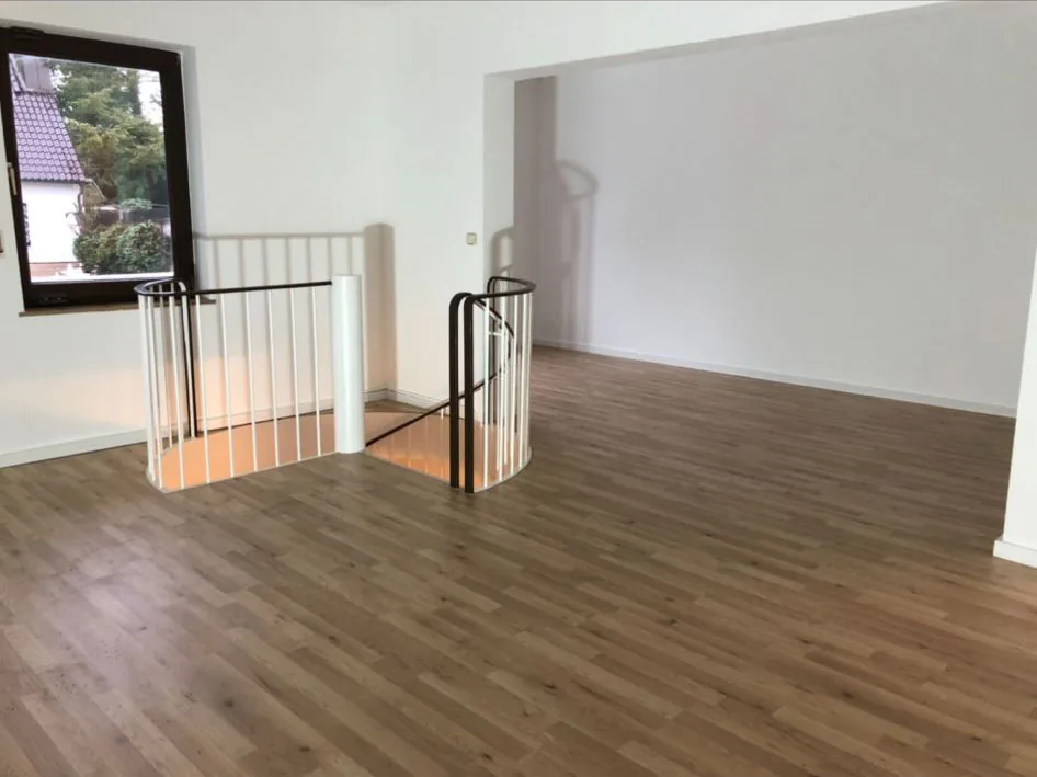 Leerer, hell gestrichener Wohnraum mit Wendeltreppe.