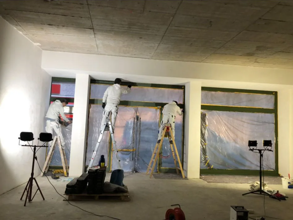 Drei Maler streichen die Innenwände eines Ladenlokals mit abgeklebter Schaufensterfront.