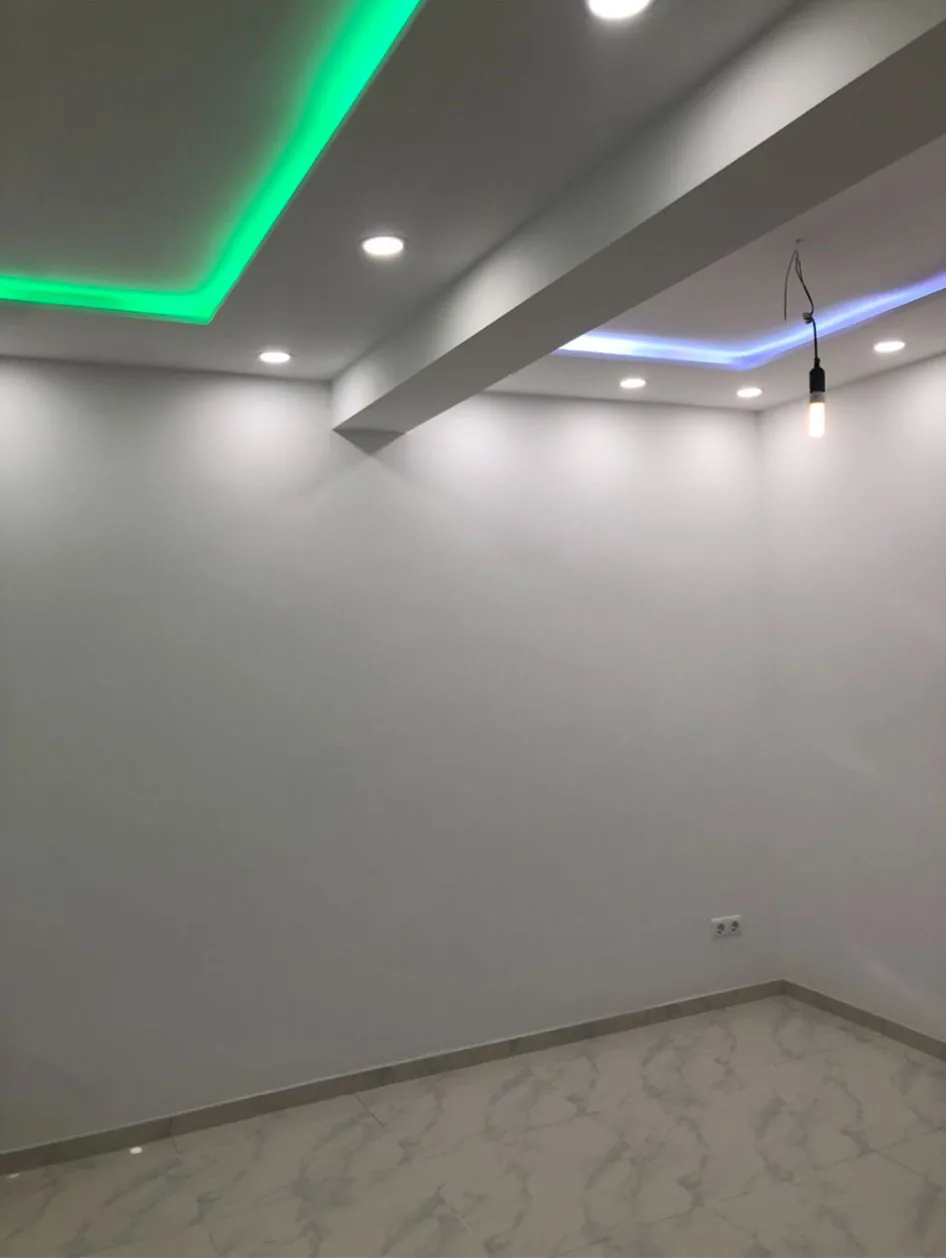 Raum mit weißen Wänden, Marmorfliesen und Lichtdecke mit farbiger LED-Beleuchtung.