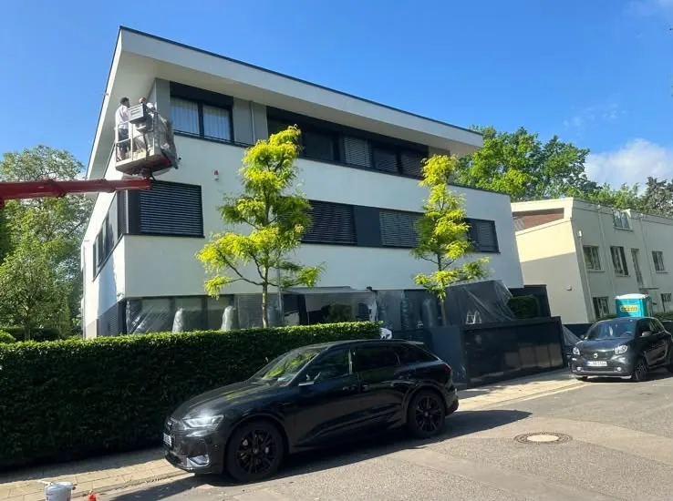 Dieselbe Stadtvilla von der Seite, zwei Maler arbeiten auf einer Hubarbeitsbühne am Obergeschoss.